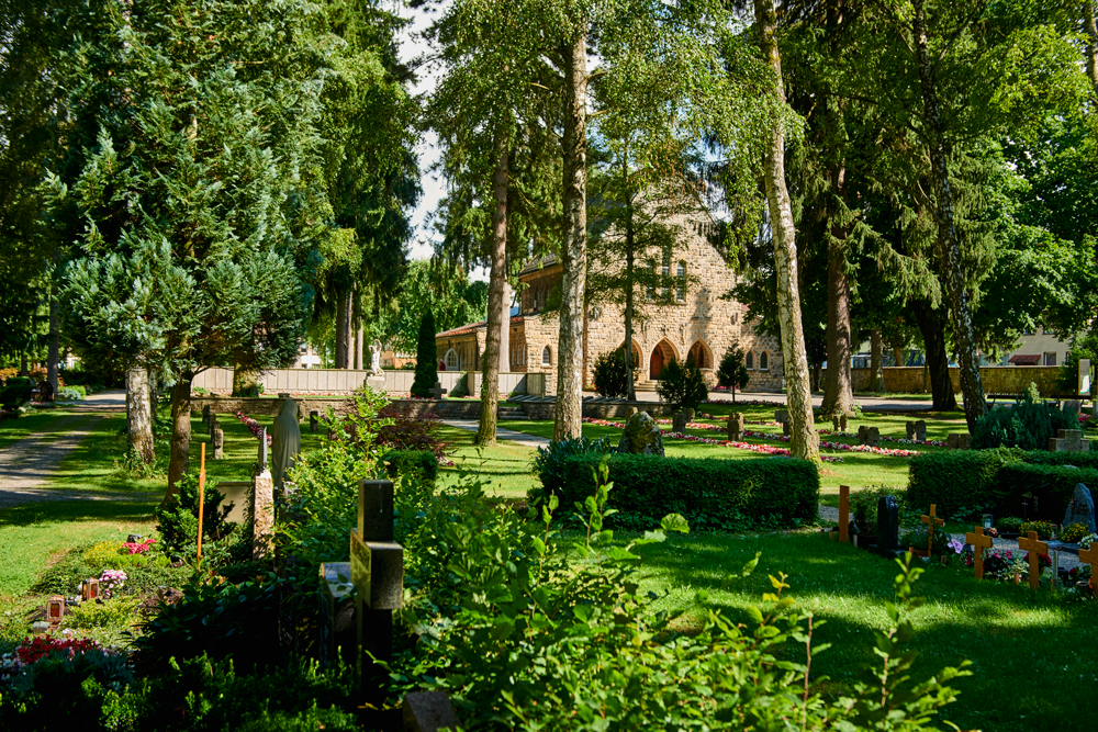 Stadtfriedhof Rottweil: Im Vordergrund sind einige Gräber zu sehen. Im Hintergrund hinter den Bäumen steht eine Kirche.